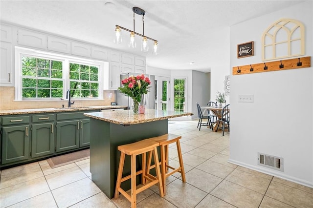 kitchen featuring a kitchen bar, visible vents, a sink, light tile patterned floors, and green cabinets