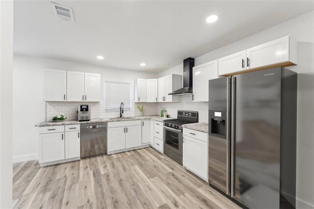 kitchen featuring wall chimney range hood, sink, light hardwood / wood-style flooring, appliances with stainless steel finishes, and white cabinets