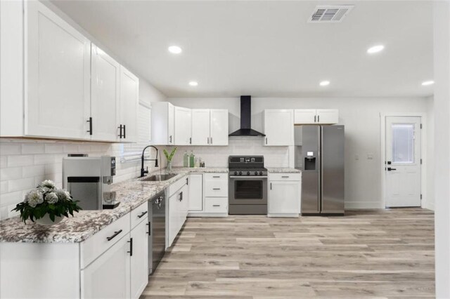 kitchen featuring appliances with stainless steel finishes, sink, wall chimney range hood, and white cabinets