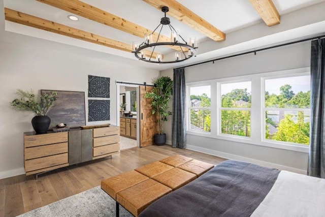 bedroom featuring ensuite bathroom, light hardwood / wood-style flooring, a barn door, beamed ceiling, and a notable chandelier