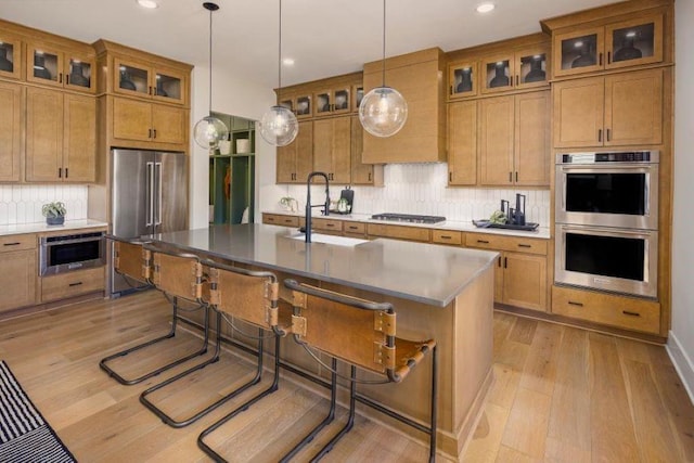 kitchen featuring a kitchen bar, appliances with stainless steel finishes, light wood-type flooring, a kitchen island with sink, and decorative light fixtures