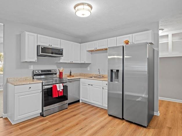 kitchen featuring sink, light hardwood / wood-style floors, a textured ceiling, white cabinets, and appliances with stainless steel finishes