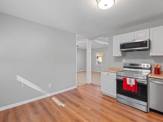 kitchen featuring white cabinets, stainless steel appliances, a textured ceiling, and light hardwood / wood-style floors