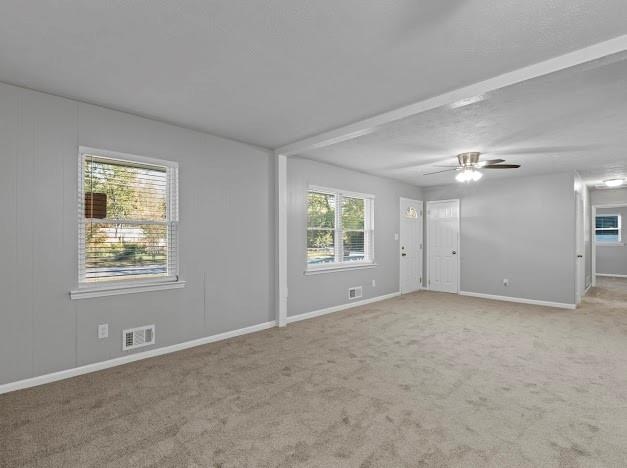 carpeted empty room featuring beamed ceiling and ceiling fan