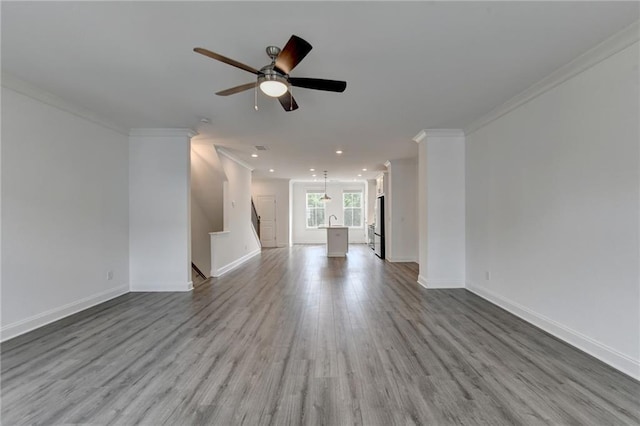 unfurnished living room with a ceiling fan, a sink, wood finished floors, crown molding, and baseboards