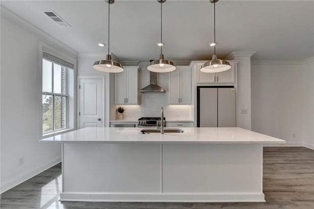 kitchen with visible vents, a center island with sink, a sink, freestanding refrigerator, and wall chimney range hood