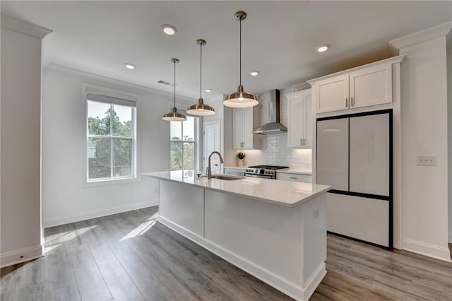 kitchen featuring a kitchen island with sink, a sink, white fridge, gas range, and wall chimney exhaust hood