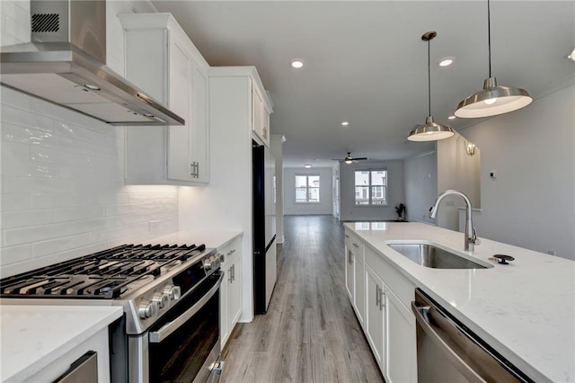 kitchen featuring a sink, appliances with stainless steel finishes, white cabinets, and wall chimney range hood