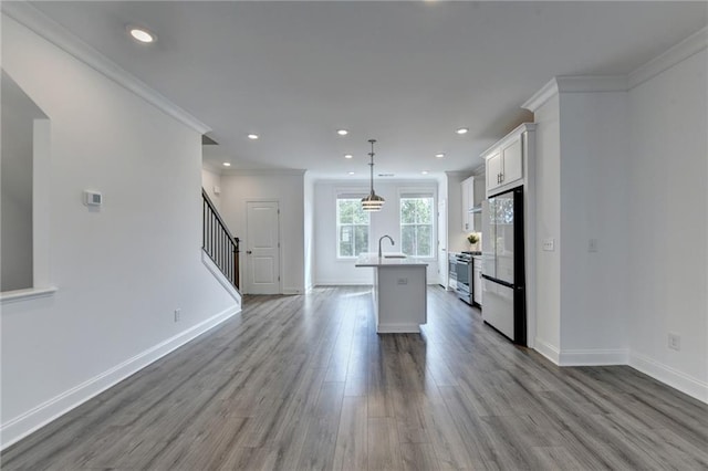 kitchen with dark wood-style flooring, gas stove, a kitchen island with sink, and freestanding refrigerator