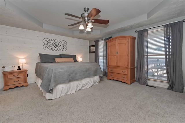 bedroom with a tray ceiling, light colored carpet, and ceiling fan