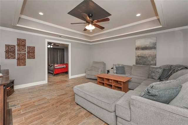 living room featuring a tray ceiling, crown molding, light wood-style flooring, a ceiling fan, and baseboards