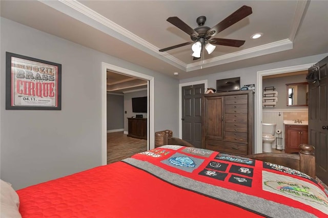 bedroom featuring ornamental molding, a tray ceiling, connected bathroom, and wood finished floors