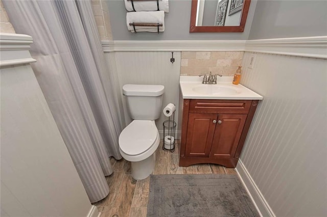 bathroom featuring curtained shower, toilet, a wainscoted wall, wood finished floors, and vanity