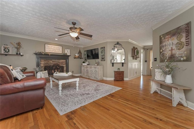 living area featuring a ceiling fan, wood finished floors, a textured ceiling, crown molding, and a fireplace