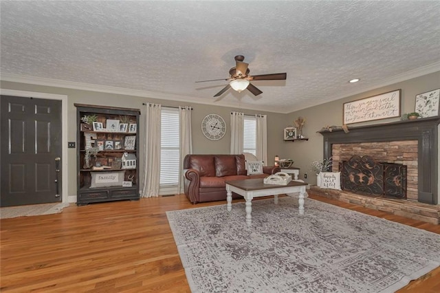 living area with a textured ceiling, a stone fireplace, wood finished floors, and crown molding