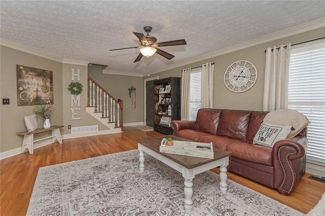 living area featuring crown molding, visible vents, a textured ceiling, wood finished floors, and stairs