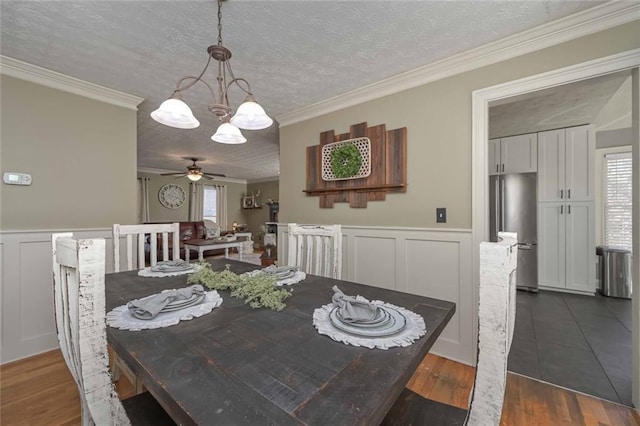 dining room with a textured ceiling, dark wood-style flooring, wainscoting, and crown molding