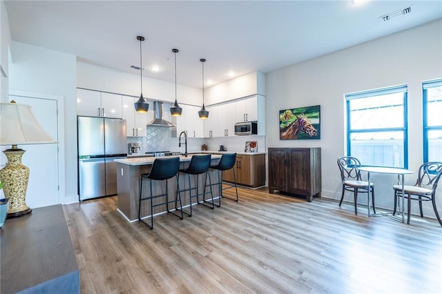 kitchen featuring white cabinets, appliances with stainless steel finishes, light countertops, a kitchen breakfast bar, and wall chimney exhaust hood