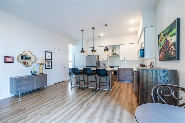 kitchen featuring wall chimney range hood, white cabinets, a breakfast bar, stainless steel appliances, and a kitchen island