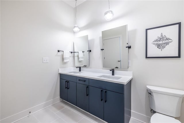 bathroom with baseboards, a sink, double vanity, and toilet