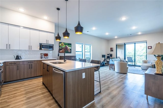kitchen featuring open floor plan, a breakfast bar area, white cabinetry, a sink, and appliances with stainless steel finishes