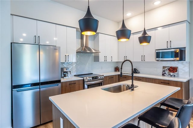 kitchen with a breakfast bar, modern cabinets, wall chimney exhaust hood, a sink, and stainless steel appliances