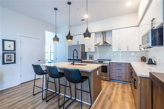 kitchen with wall chimney range hood, stainless steel appliances, a breakfast bar, and light wood-style floors