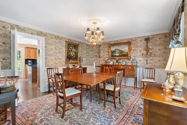 dining space with wallpapered walls, a chandelier, a wainscoted wall, wood finished floors, and crown molding