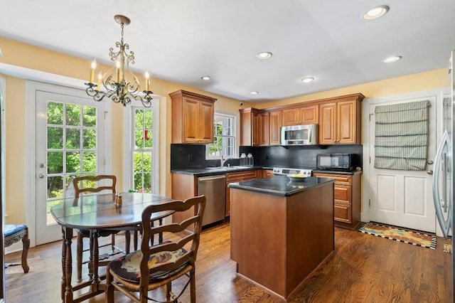 kitchen with appliances with stainless steel finishes, dark countertops, a chandelier, a center island, and tasteful backsplash