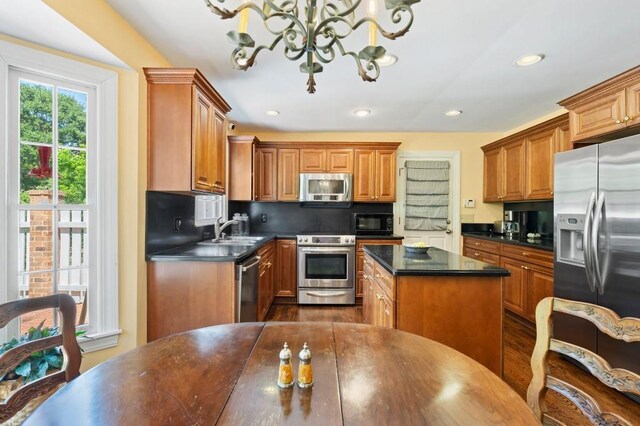 kitchen featuring stainless steel appliances, dark countertops, a sink, a chandelier, and brown cabinetry