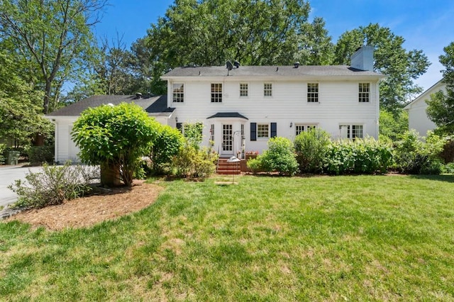 rear view of house featuring a chimney, a yard, a garage, and concrete driveway