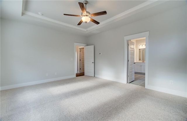 unfurnished bedroom featuring a ceiling fan, a tray ceiling, connected bathroom, carpet flooring, and baseboards