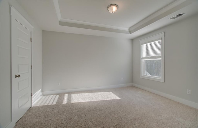 carpeted spare room featuring visible vents, a raised ceiling, baseboards, and crown molding