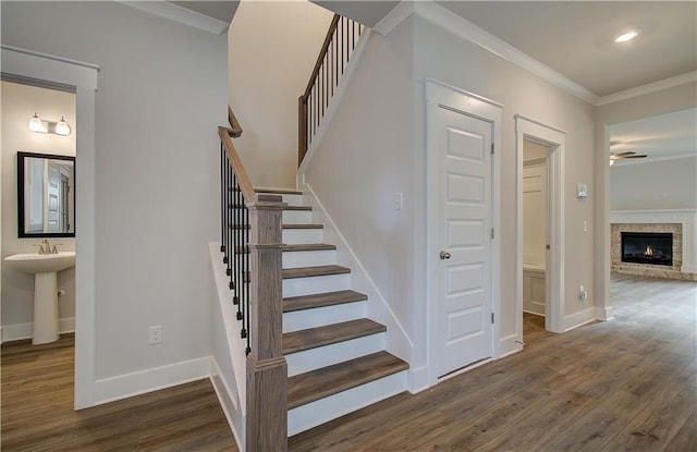 stairs with a glass covered fireplace, wood finished floors, baseboards, and ornamental molding