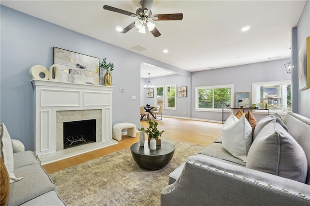 living room featuring a tile fireplace, ceiling fan with notable chandelier, and light hardwood / wood-style floors