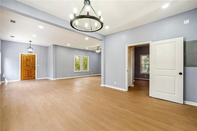 unfurnished living room featuring ceiling fan with notable chandelier and light hardwood / wood-style flooring