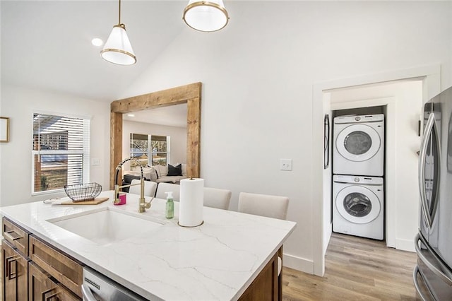 kitchen featuring lofted ceiling, stainless steel appliances, a sink, light wood-type flooring, and stacked washer and clothes dryer