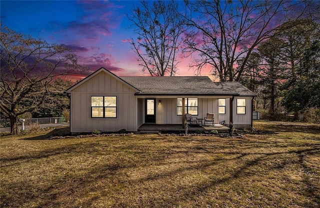 view of front facade with covered porch, a yard, board and batten siding, and fence