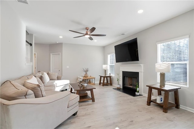 living area with light wood-style flooring, recessed lighting, a ceiling fan, and a fireplace with raised hearth