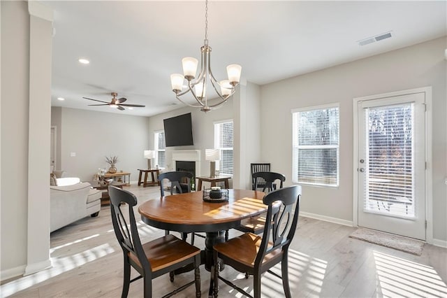 dining space featuring visible vents, baseboards, light wood-type flooring, ceiling fan with notable chandelier, and a fireplace