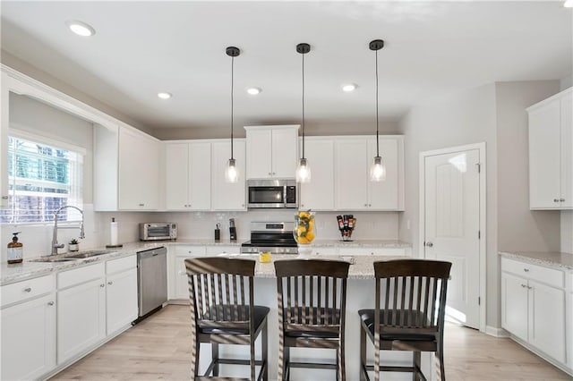 kitchen with a kitchen island, appliances with stainless steel finishes, a kitchen breakfast bar, white cabinets, and a sink