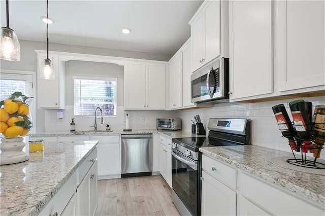 kitchen with tasteful backsplash, appliances with stainless steel finishes, light wood-style floors, white cabinets, and a sink