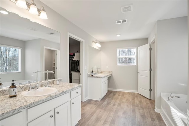 full bathroom with a garden tub, wood finished floors, visible vents, and a sink