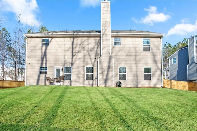 rear view of property with a yard, a chimney, and fence