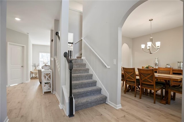 staircase featuring arched walkways, baseboards, an inviting chandelier, and wood finished floors