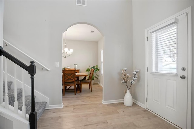 entrance foyer featuring visible vents, baseboards, light wood-type flooring, an inviting chandelier, and arched walkways