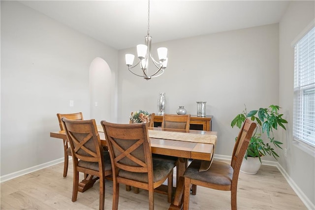 dining room featuring light wood-type flooring, arched walkways, a notable chandelier, and baseboards