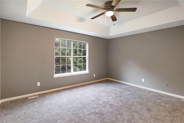 spare room with a ceiling fan, carpet, a raised ceiling, and baseboards