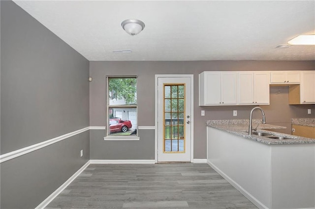 kitchen featuring light wood finished floors, white cabinetry, baseboards, and a sink