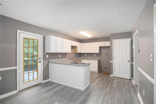 kitchen with a peninsula, light wood-style flooring, white cabinetry, and a sink